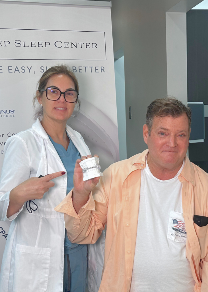 A woman in a lab coat and glasses proudly points to a smiling man holding a white container. They stand beside a "Sleep Center" sign, conveying a sense of achievement.